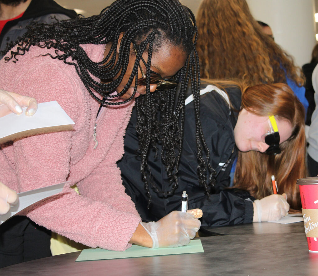 Students attempt to write a letter wearing gloves and sunglasses to simulate the impairments