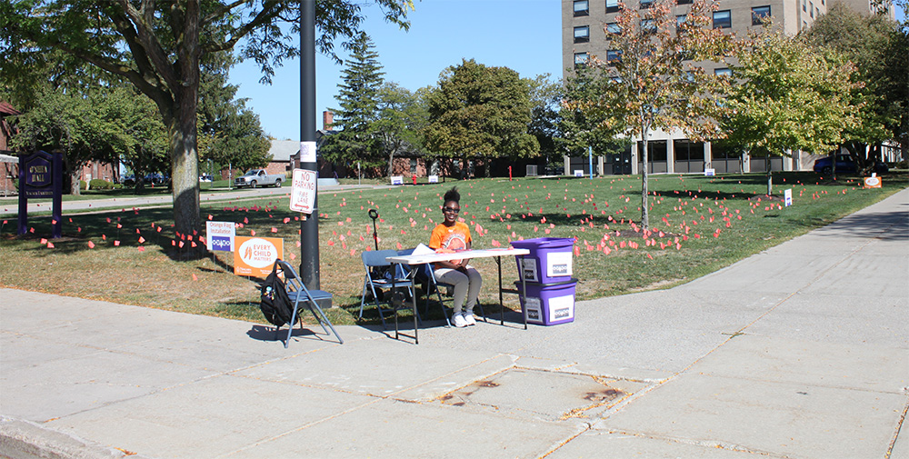Symyah Simeus of Niagara University’s Intercultural Engagement Center staffs a table during an orange flag installation