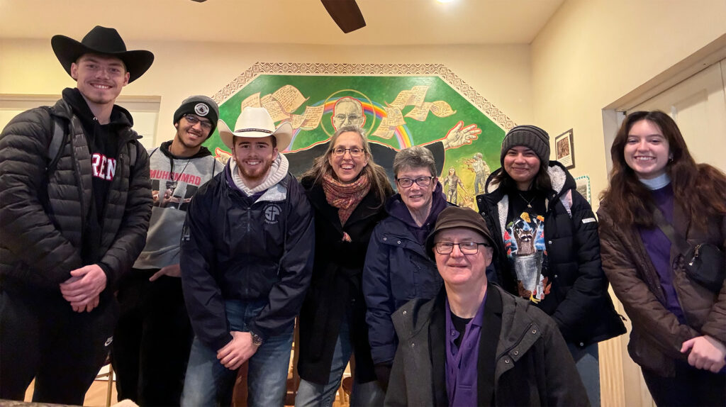 Henry Brophy, Nikaulas Smith-Goddard, Mateo Gruosso, program director Beth Riehle, Sr. Nora Gatto, D.C., Fr. Greg Semeniuk, C.M., Marianne Bonilla, and Ava Palo at the St. Columban Mission Center in front of an image of St. Oscar Romero, former archbishop of San Salvador and martyr.