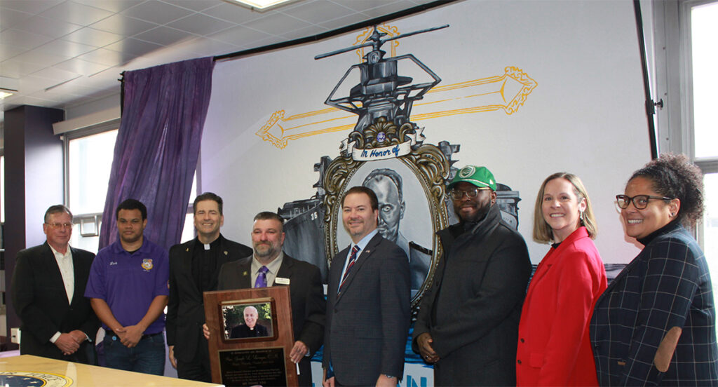 From left, Robert Healy, inaugural director of Niagara University’s Veterans Services program; veteran and NU student Zechary Fisher, ’27; Rev. James J. Maher, C.M., Niagara University president; Karl Hinterberger, director of the Veterans Services program; NYS Senator Robert Ortt; artist Tyshaun D. Tyson; Jaclyn Rossi Drozd, ’08, M.S.Ed.’10, vice president for institutional advancement; and Brandi Alfiero, program manager at Foundation 214, in front of the mural of Rev. Lt. Thomas M. Conway, a Navy chaplain and Niagara University alumnus.