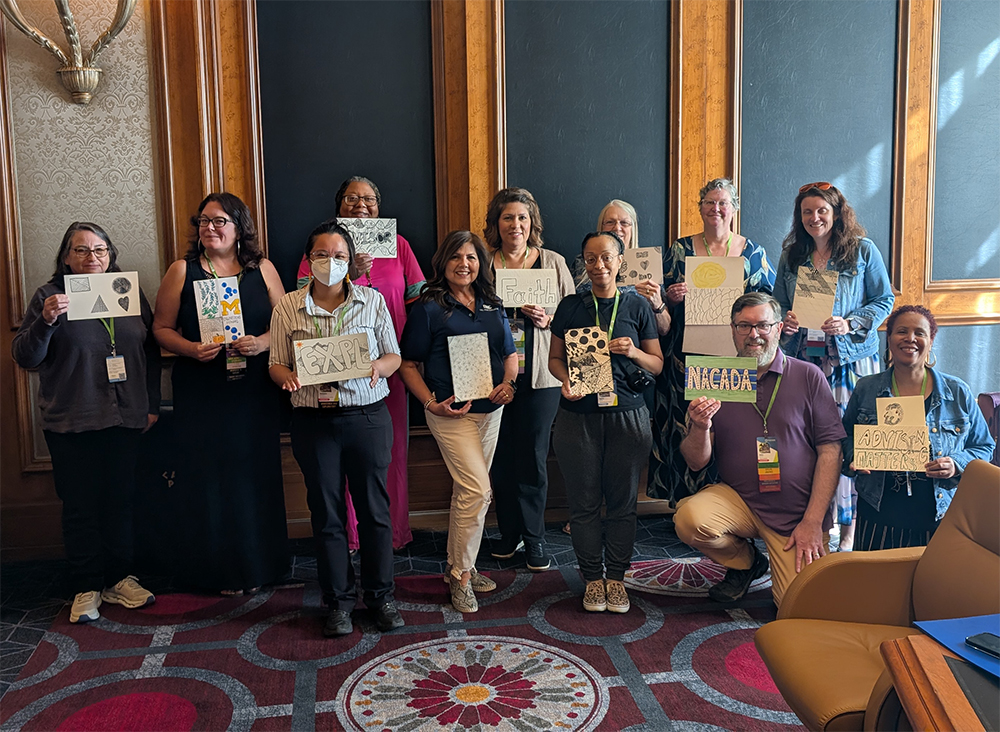 A group of people in a conference room holding artwork they created.