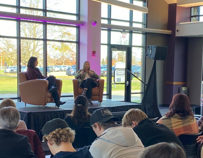 Two women on stage in front of audience of students