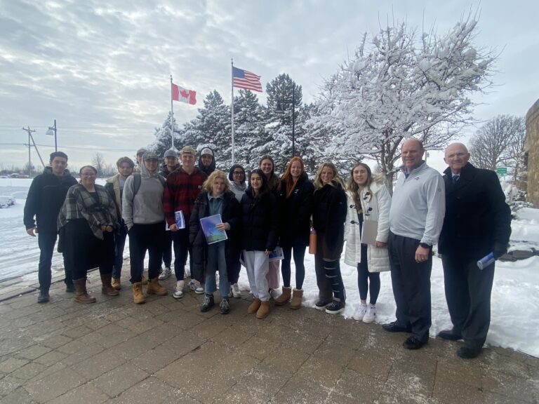 Students and faculty in front of American and Canadian flags