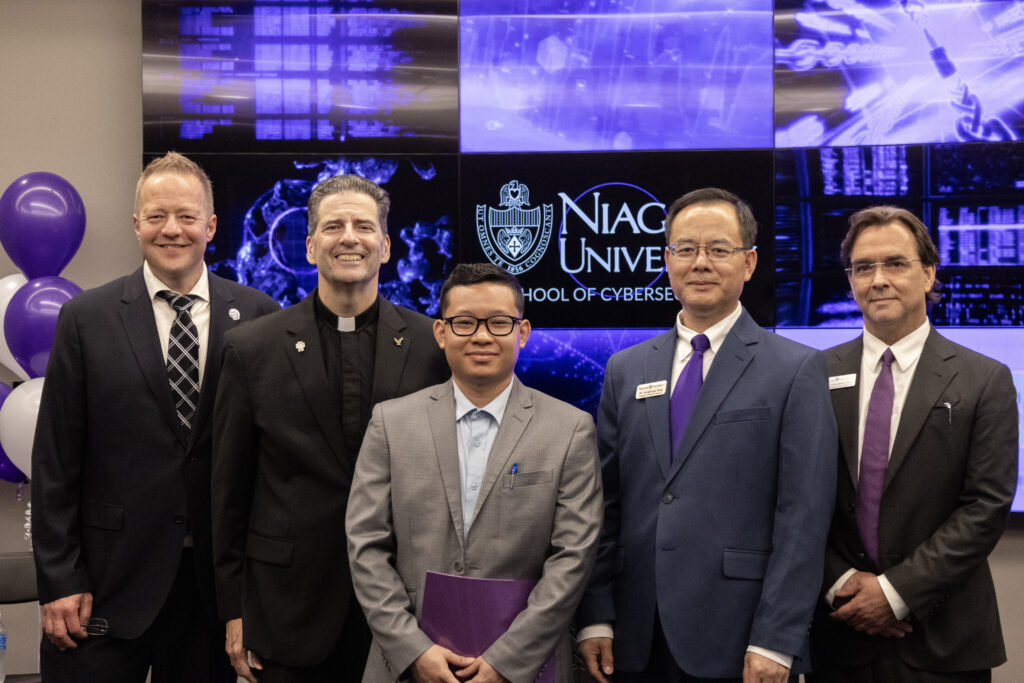 image of Father James J. Maher with four other people. Including Elher Tha, Petter Lovaas, Mark Frascatore standing in front of a digital screen.