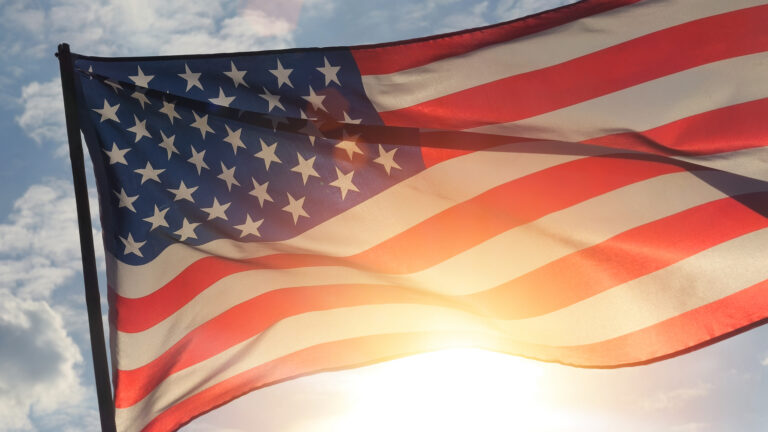 close up of the american flag waving in the wind with the sun behind it