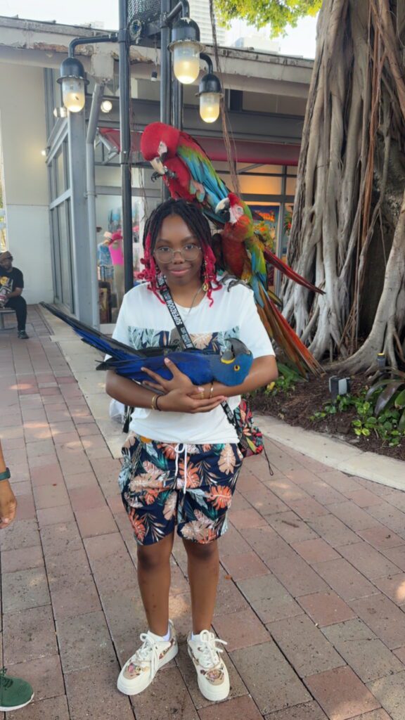Qierra Gregory posing with 3 parrots. Two are on her shoulders, one is in her arms.