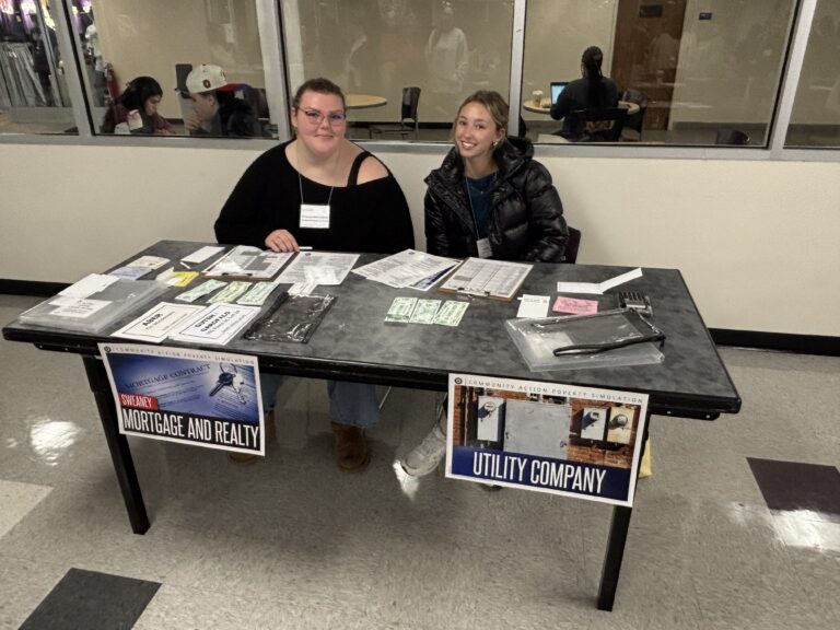 Two students participating at a services table within the Community Action Poverty Simulation